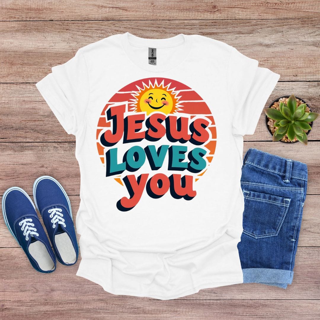 White t-shirt with 'Jesus Loves You' design on a wooden surface with shoes and jeans.