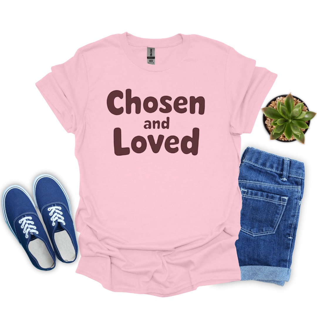 Pink t-shirt with 'Chosen and Loved' text, blue sneakers, jeans, and a plant on a white background