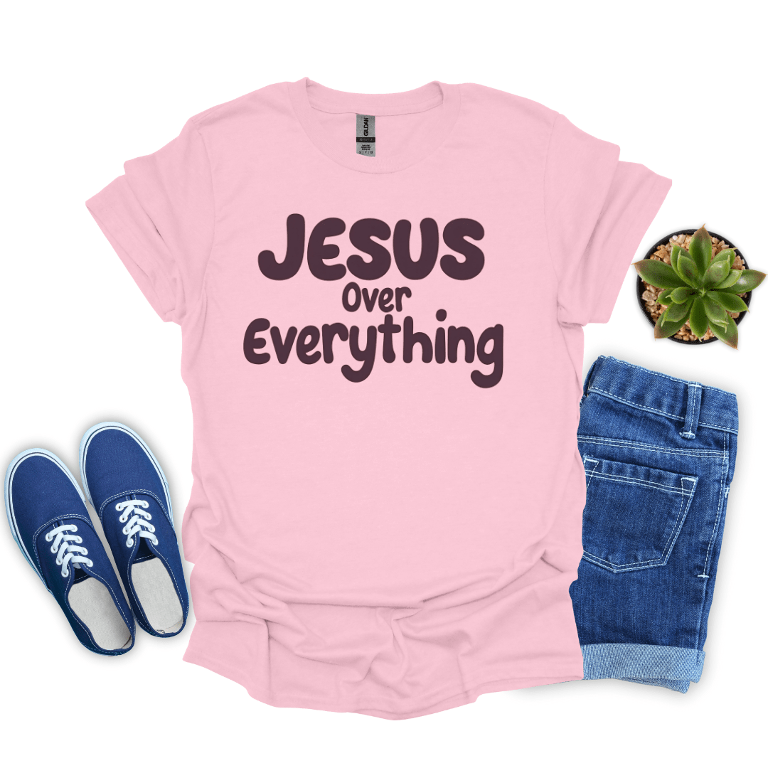 Pink t-shirt with 'Jesus Over Everything' text, blue sneakers, and jeans on a white background