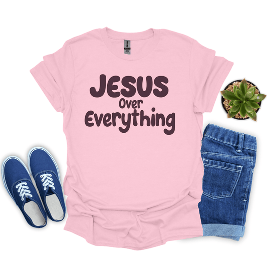 Pink t-shirt with 'Jesus Over Everything' text, blue sneakers, and jeans on a white background