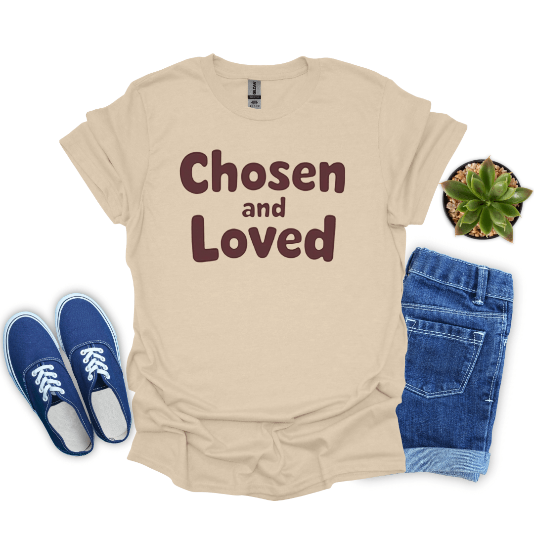 Sand t-shirt with 'Chosen and Loved' text, blue sneakers, and jeans on a white background