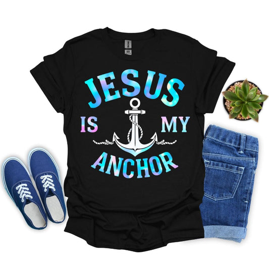 Black t-shirt with 'Jesus is my anchor' design, blue sneakers, denim shorts, and a plant on a white background.