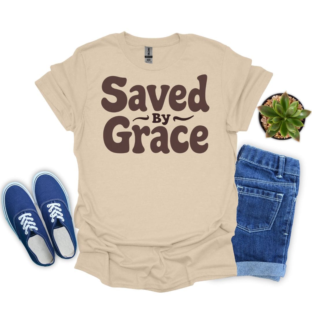 Sand t-shirt with 'Saved by Grace' text, blue sneakers, denim shorts, and a plant on a white background