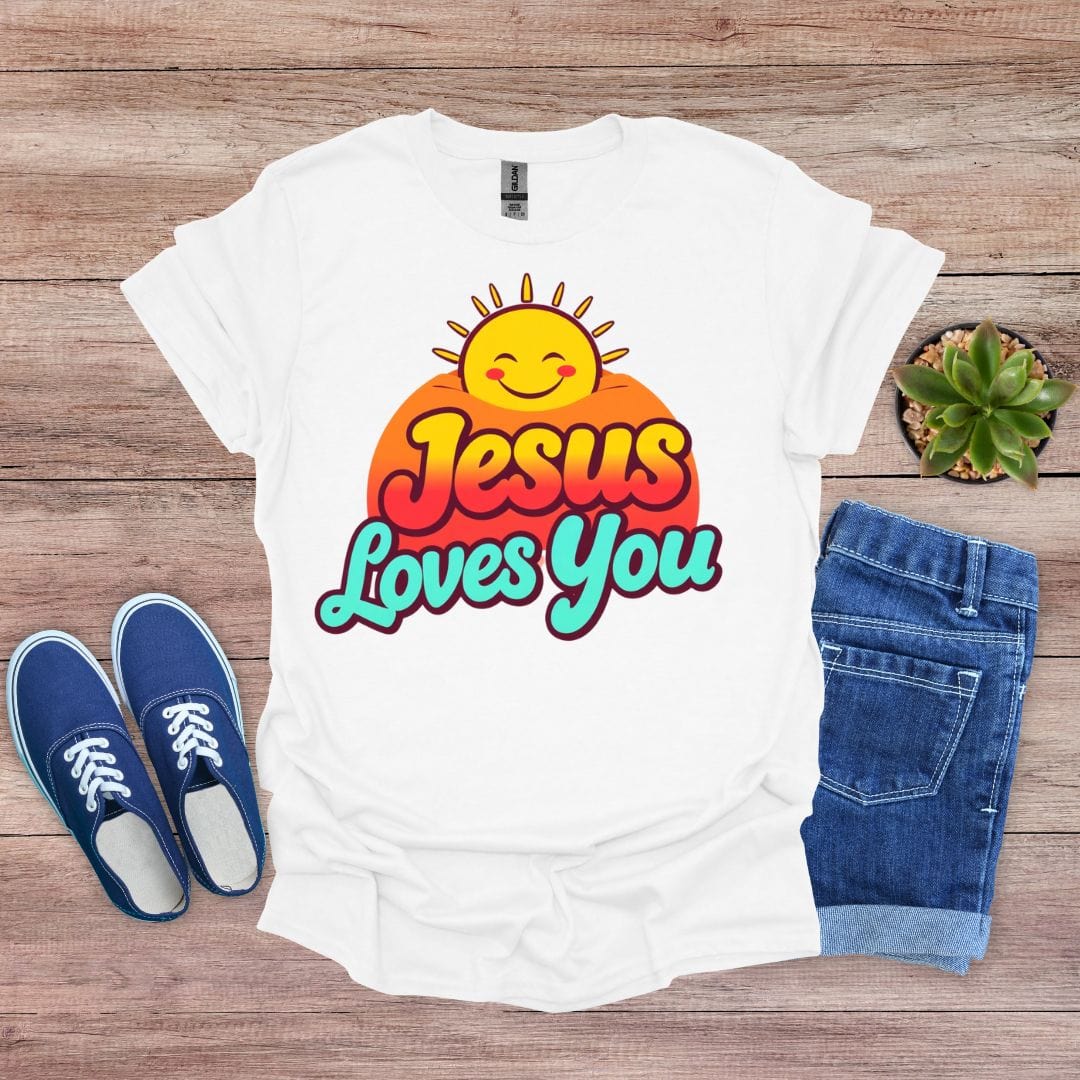 White t-shirt with 'Jesus Loves You' design on a wooden surface with shoes and jeans.