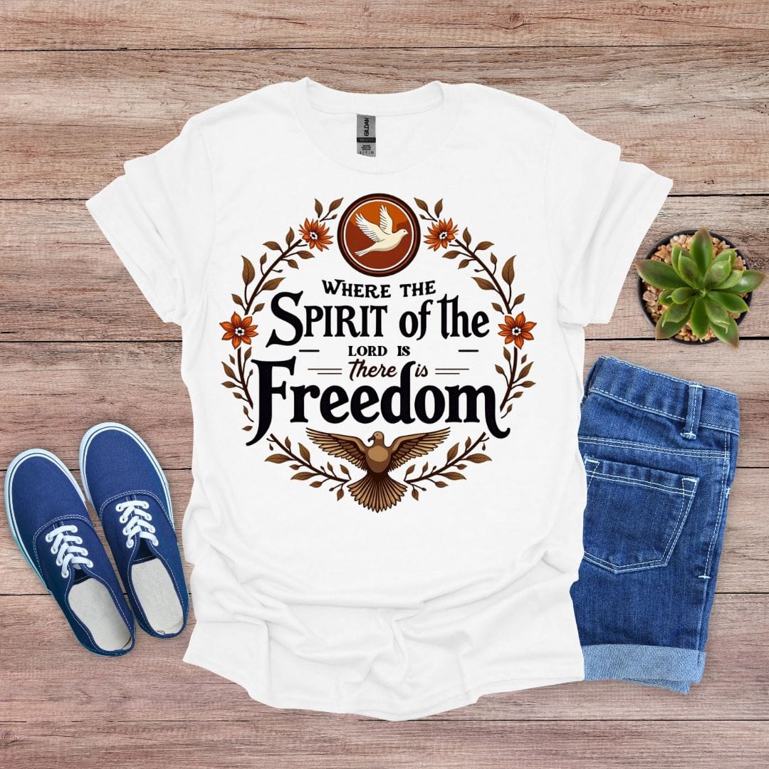 White t-shirt with 'Where the Spirit of the Lord is, there is Freedom' design on a wooden surface with blue shoes and jeans.